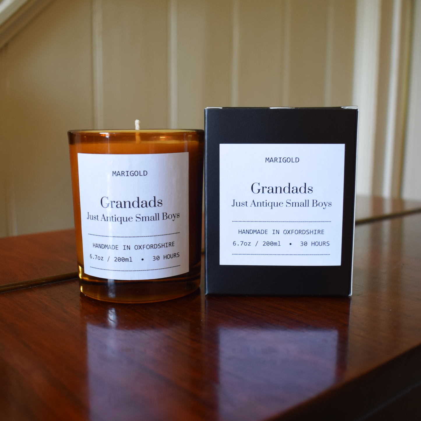 Candle and packaging labeled 'Grandads Just Antique Small Boys' by Marigold on a wooden surface.