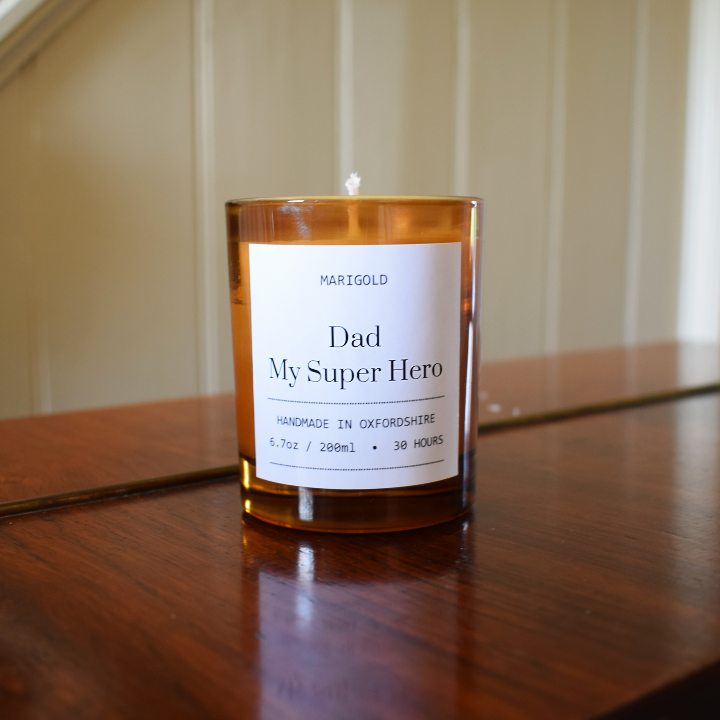 Candle with a label reading 'Dad My Super Hero' on a wooden surface.