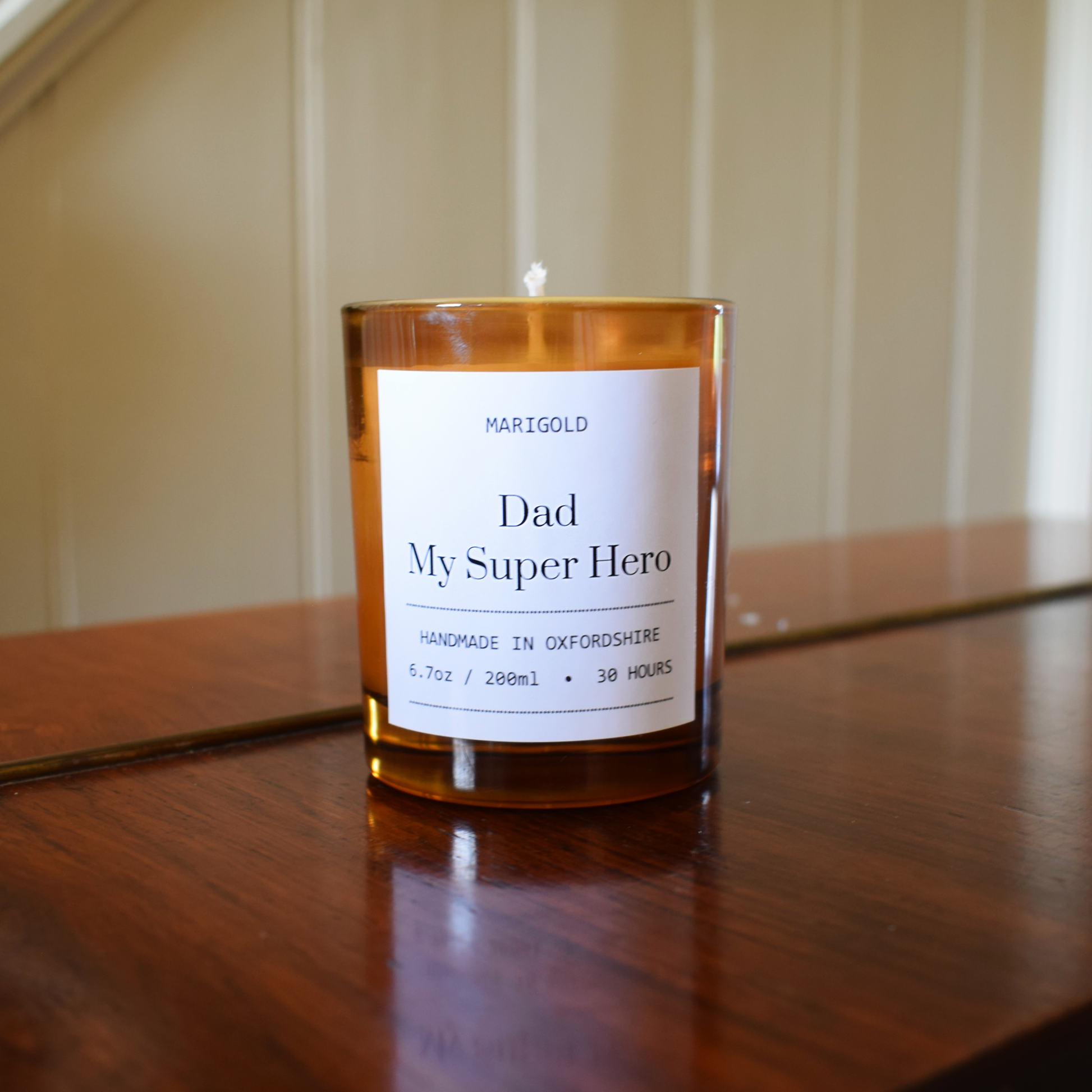 Candle with a label reading 'Dad My Super Hero' on a wooden surface.