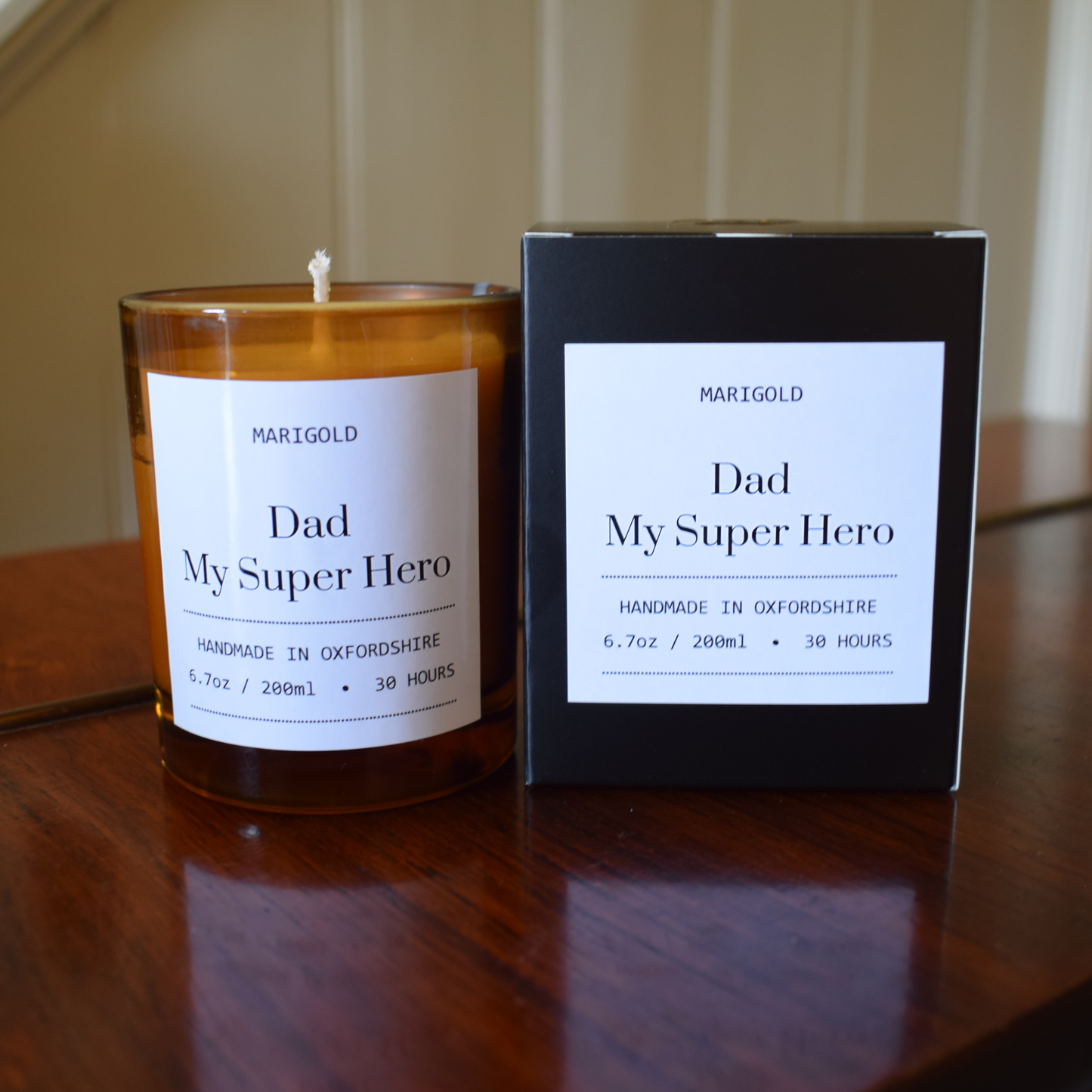 Candle and packaging labeled 'Dad, My Super Hero' by Marigold on a wooden surface.