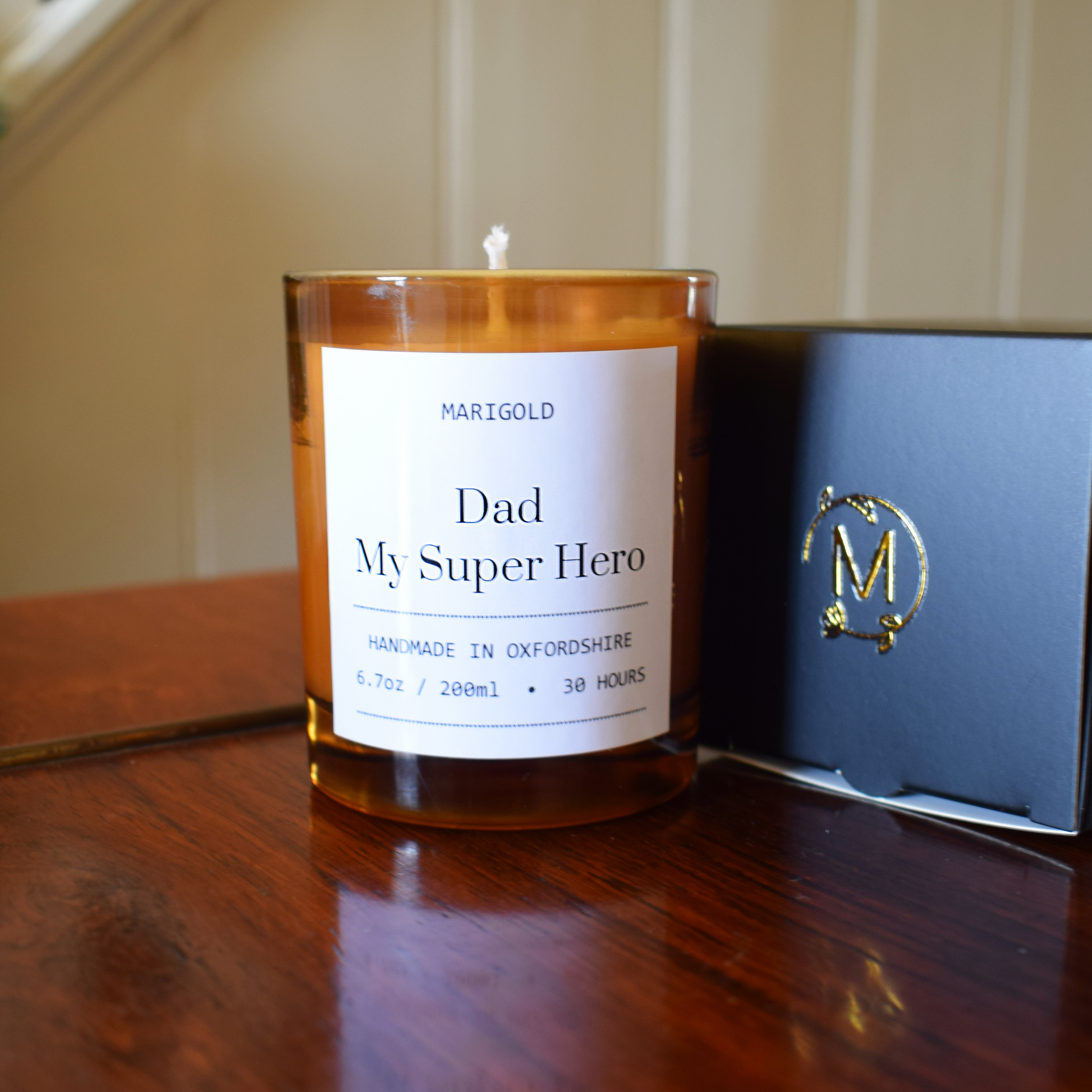 Candle with 'Dad My Super Hero' label next to a box on a wooden surface