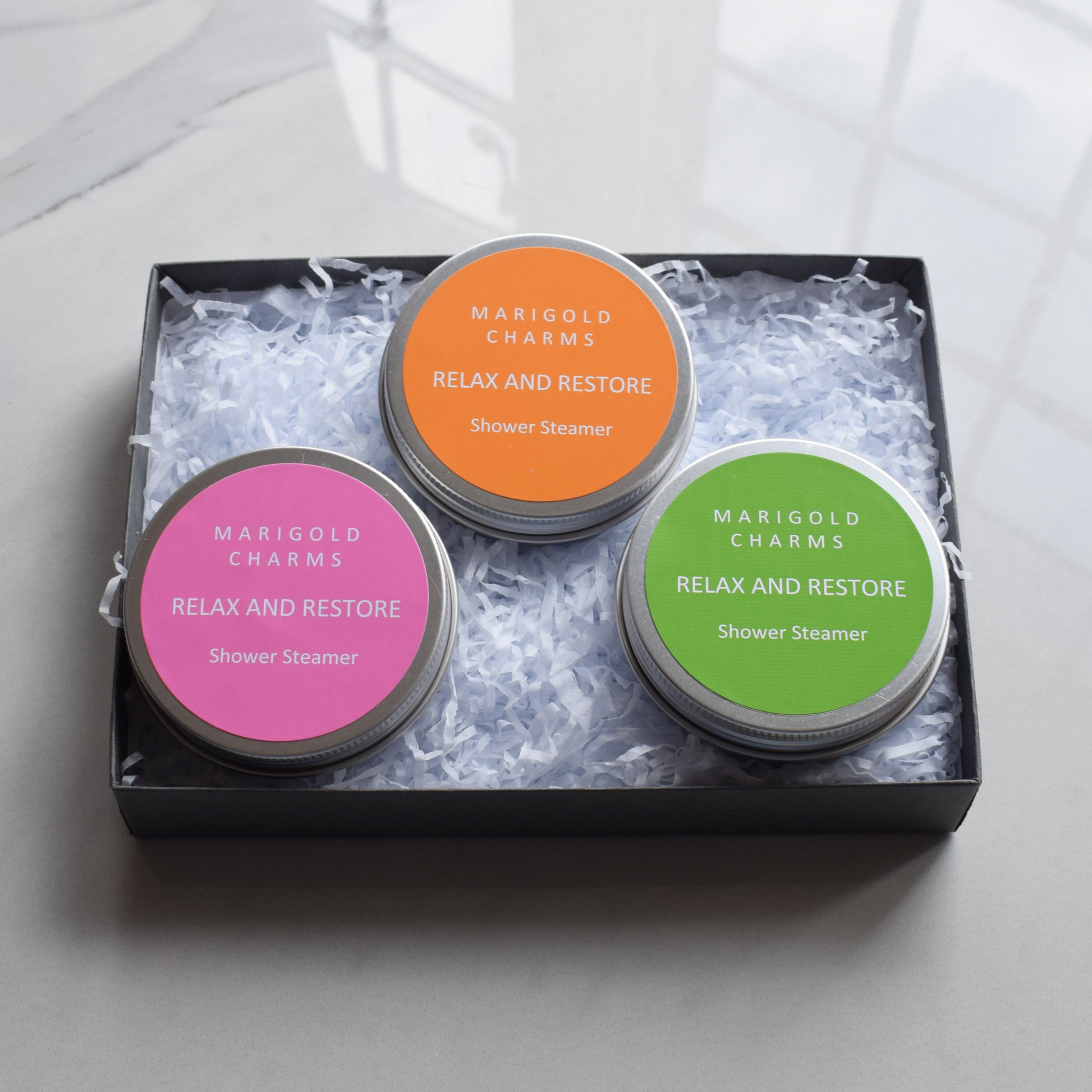Three shower steamer  in a gift set with colorful labels in a black box on a light grey background