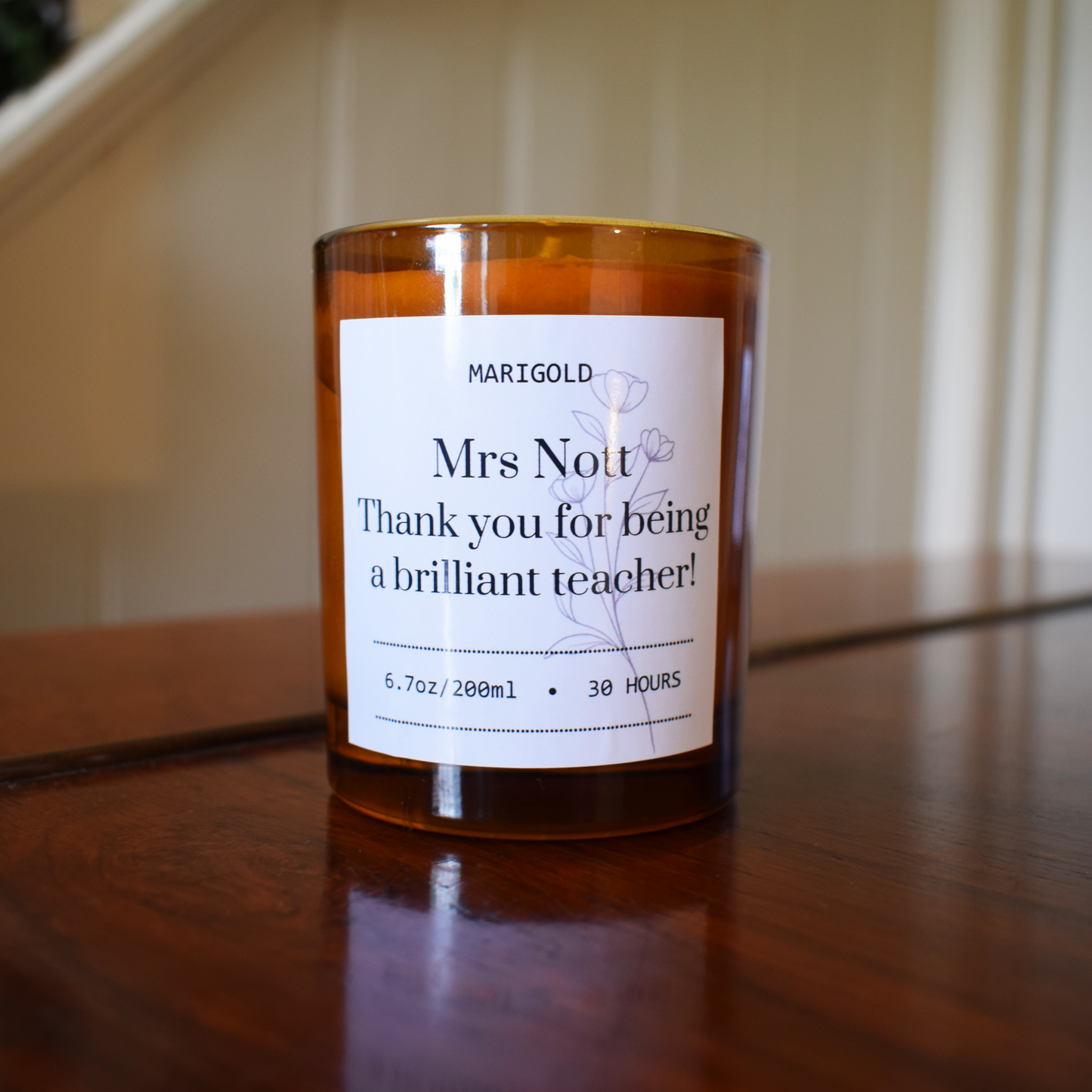 Thank you Teacher Candle in an amber glass with a white label on a wooden surface