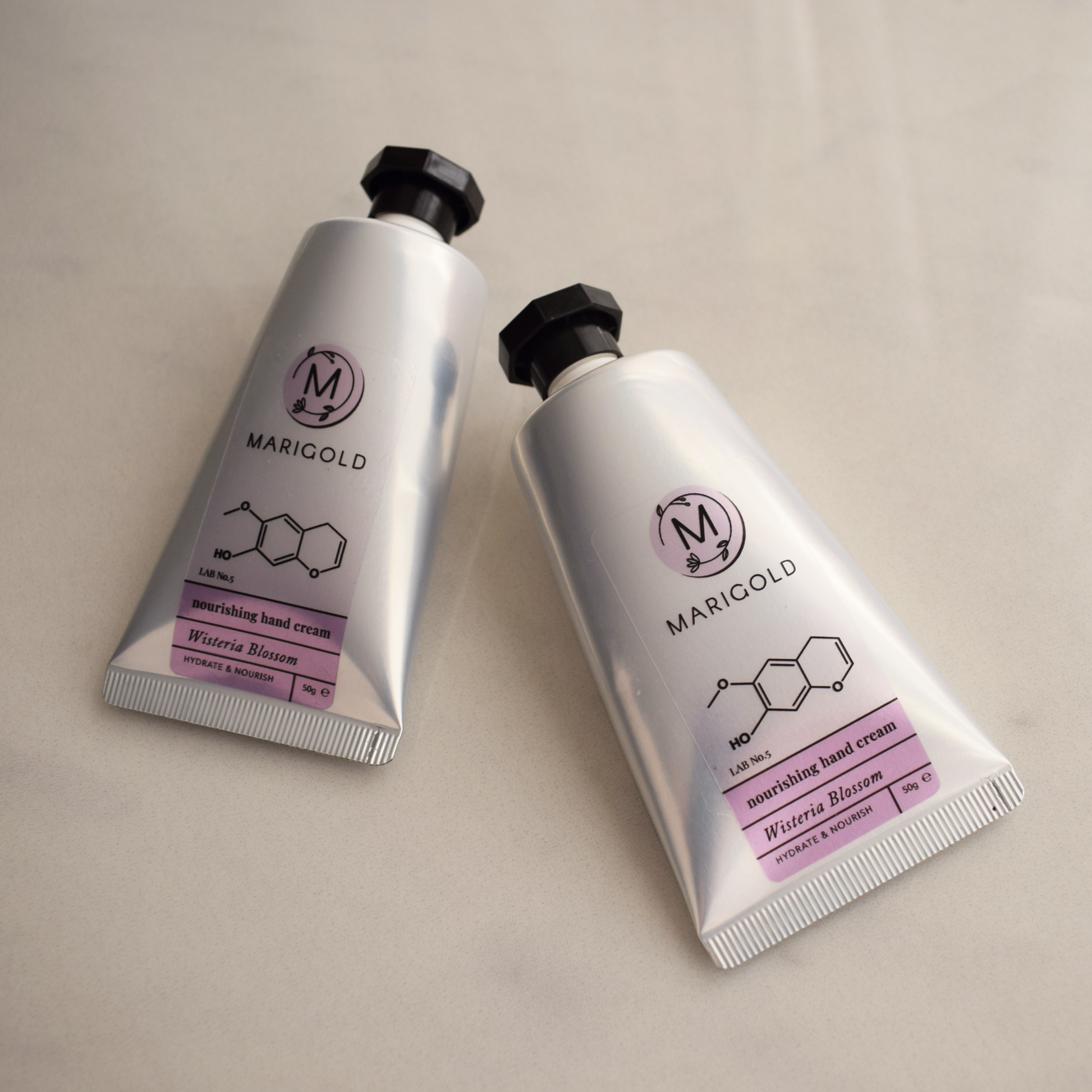 Two silver Wisteria hand cream tubes with purple labels on a beige background